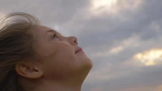 Close-up of pensive face of girl with open eyes. child looks up to the sky. Portrait of little girl looking at sky dreaming. Pensive look of child. Child's face, sad look.