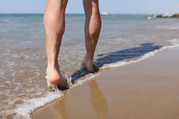 Man feet walking along sandy beach closeup