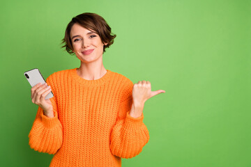 Photo of brown bob haired young pretty woman point thump empty space hold phone isolated on green color background