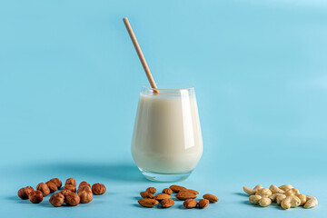 Glass of organic vegan dairy free milk from nuts. Healthy breakfast with vegetarian alternative drink. Various types of nuts: cashew, hazelnuts, almonds on blue background. Copy space for text.