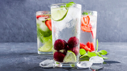Three glass of refreshing cool detox drink with strawberry, lime, cherry and mint on blue background. Various summer lemonades or ice tea. Mojito cocktails with ice cubes. Healthy eating.