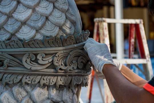 Close-up hand of Myanmar skilled artisan while using mortar concrete making a large great naga statue.