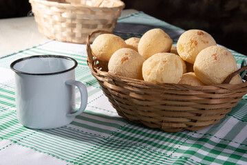 Cheese bread, straw basket full of cheese bread and a white cup on a checkered tablecloth, selective focus.