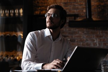 Handsome young freelancer is having a coffee break and dreaming after working with a laptop at the coffee shop.