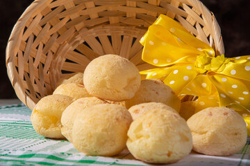 Cheese bread, straw basket with a bow of yellow ribbon fallen with cheese bread on a checkered tablecloth, selective focus.