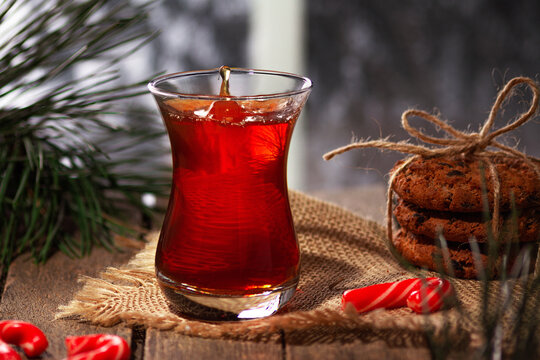 A drop of tea falls into a glass beaker. Armuda with tea. Hot tea on a winter evening. Tea with cookies and Christmas sweets. Selective focus.