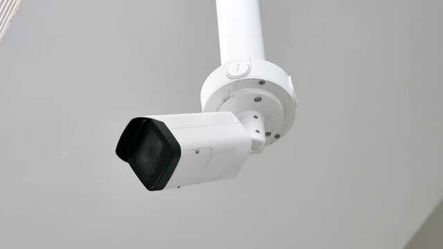 CCTV, Single white surveillance camera hanging from the celling closeup, detail, side view. Spying, monitoring, controlling, public space or corporate area safety, protection abstract concept, nobody