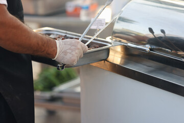 Chef in rubber gloves holding metal tray with food and tongs closeup
