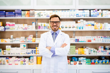 Portrait of smiling caucasian pharmacist standing in drug store with arms crossed.