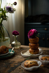 Homemade cherry and chocolate muffins and ranunculus and anemone flowers on rustic wooden table. 