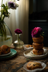 Homemade cherry and chocolate muffins and ranunculus and anemone flowers on rustic wooden table. 