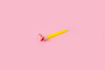 Rolled festive noisemaker or party whistle horn over pink background