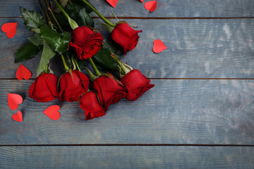 Beautiful red roses and paper hearts on blue wooden background, flat lay with space for text. Valentine's Day celebration