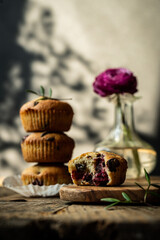 Bitten homemade cherry and chocolate muffin on wooden board with stack of three muffins on background .