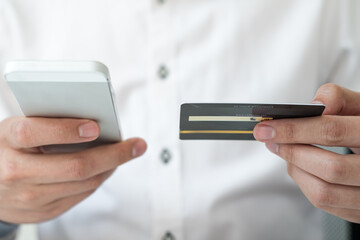 The businessman's hand is holding a credit card and using a smartphone for online shopping and internet payment in the office