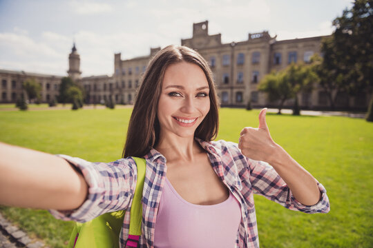 Photo of charming happy young woman make thumb up selfie camera wear plaid shirt outside in campus outdoors
