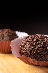 Brigadeiros, traditional Brazilian sweet in detail on wooden surface, black background, selective focus.