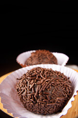 Brigadeiros, traditional Brazilian sweet in detail on wooden surface, black background, selective focus.