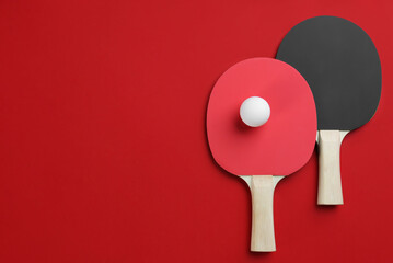Ping pong rackets and ball on red background, flat lay. Space for text