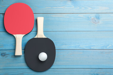 Ping pong rackets and ball on light blue wooden table, flat lay. Space for text