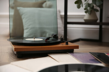 Stylish turntable with vinyl records on floor indoors