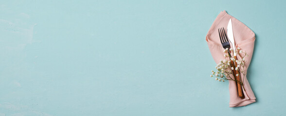 Tableware setting with fork, knife, napkin and flower on blue background,