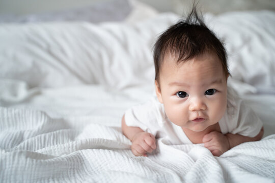 happy asian baby infant learning to crawl on white soft bed. 3 months old baby facial expression. lovely and smile baby. cute kid looking at camera.