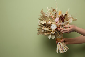 Woman holding beautiful dried flower bouquet on green background, closeup. Space for text