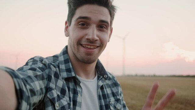 A smiling man wearing shirt is taking- selfie photo standing at the electric windmill farm