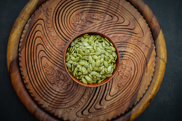 Top view of sunflower seeds in a wooden bowl on a wooden dark background.