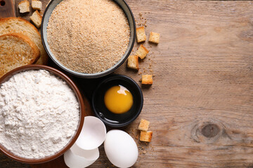 Fresh breadcrumbs, flour and eggs on wooden table, flat lay. Space for text