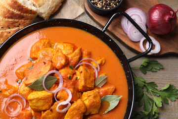 Delicious chicken curry in pan on wooden table, flat lay