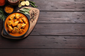 Delicious chicken curry in pan on wooden table, flat lay. Space for text