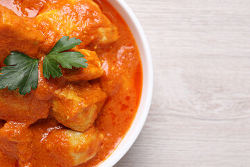 Bowl of delicious chicken curry on white wooden table, top view. Space for text