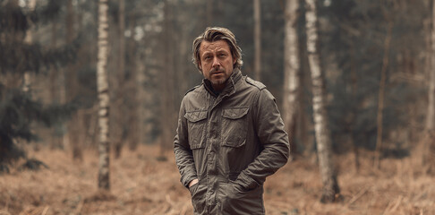 Blonde rugged man in green coat in woodland.