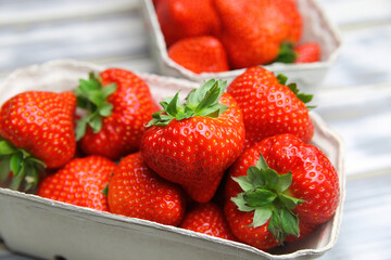 Closeup of isolated ripe fresh strawberries from german farmers market in cardboard box on white wood table