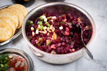 Vegan  chopped beet salad with nuts and green onion served in steel bowl on marbel surface, along with crackers