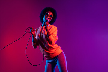 Fototapeta na wymiar Photo of carefree dark skin lady hold mic cable singing have good mood isolated on vivid color background