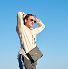 A Caucasian man from Spain wearing a black purse, glasses and a beige shirt on clear sky background