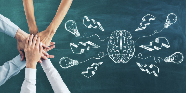 Brainstorming and teamwork concept with six hands on green chalkboard and brain hemispheres and light bulbs with lightning icons.