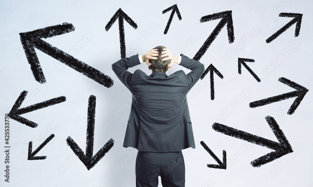 Poster difficult decision concept with man in black suit grabs his head in front of white wall with arrows 