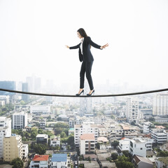 Businesswoman balancing on a string over the city, city view with scyscrapers in the background. Risk and self confidence concept