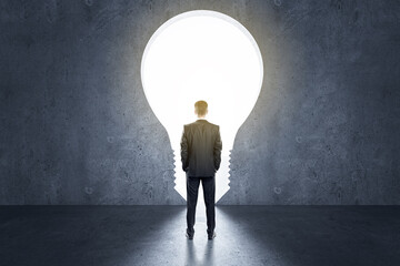 Obraz premium Startup and idea concept with back view on businessman in front of light bulb entrance in room
