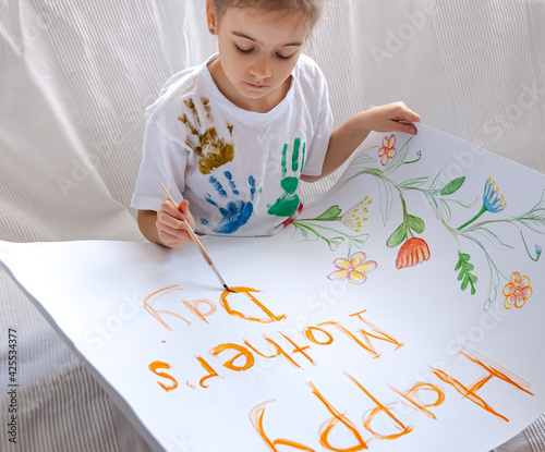 A little girl draws with paints a festive greeting card for mother's day.
