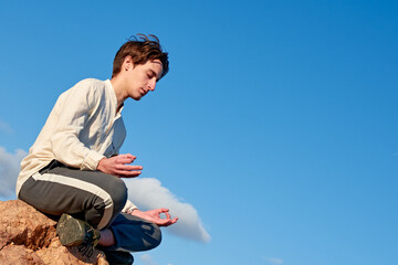 A dutch angle shot of a Caucasian man from Spain meditating on a rock on cloudy sky background