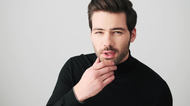 A confident man is looking at himself to the mirror standing isolated over a white wall in a studio