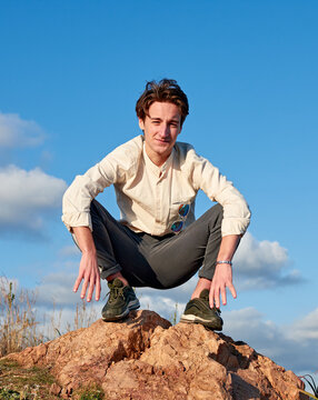 A Caucasian man from Spain squatting on a rock surrounded by grass