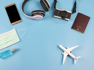 flat lay of airplane model, passport, camera, headphones, mobile phone and protective face mask and alcohol spray  on blue background.