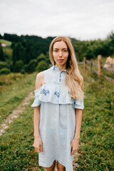Fototapeta premium Young attractive elegant blonde girl in blue romantic dress posing in the countryside