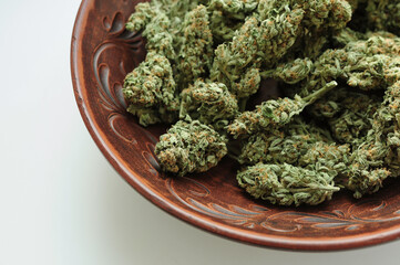 Cannabis buds in brown clay dish, flat lat, top view. Marijuana flowers close-up. Hemp recreation,...